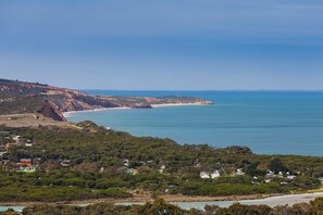 Paisatge costaner amb platja, penya-segats i una zona forestal amb edificis.