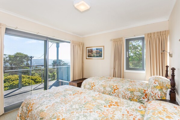 A bedroom with a large window, a bed with floral bedding, a nightstand, and a framed picture on the wall. - Anglesea Outlook (Anglesea)