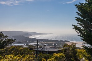 A coastal landscape with a view of the sea, hills in the distance, and a building with a flat roof in the foreground. - Anglesea Outlook (Anglesea)