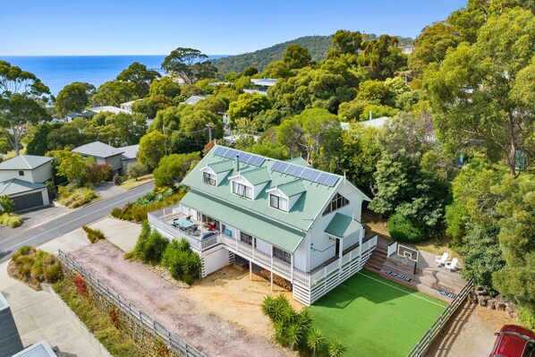 A residential property with a green-roofed house, a tennis court, and a view of the sea.