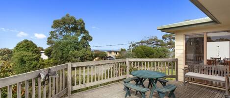 A wooden deck with a table and benches, overlooking a residential area with trees and houses.