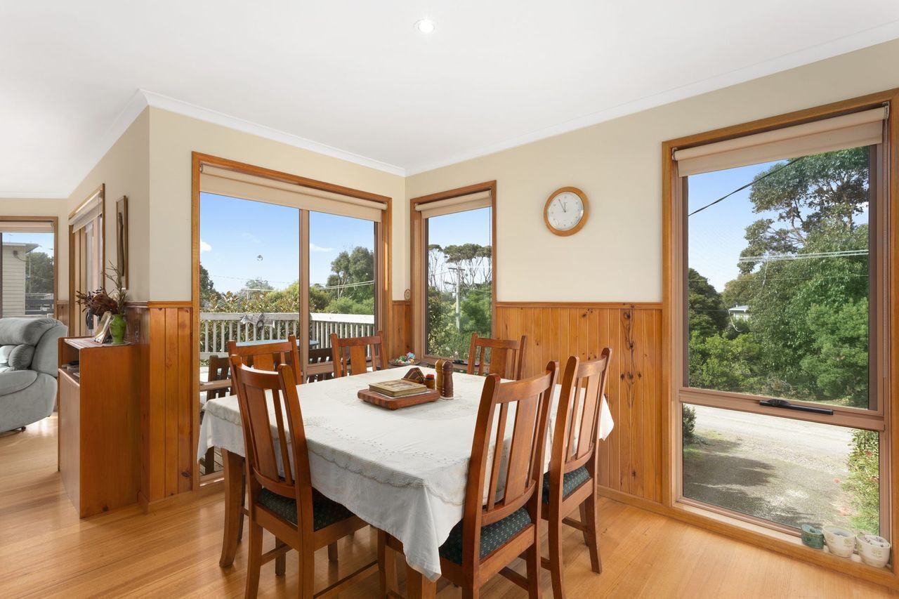 Un coin repas avec une table dressée pour quatre personnes, des chaises en bois, une nappe blanche et une horloge au mur.