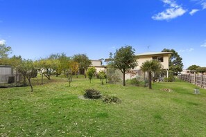 A residential property with a well-maintained lawn, a variety of trees, and a two-story house with a visible satellite dish. - Magnolia (Skenes Creek, Apollo Bay)