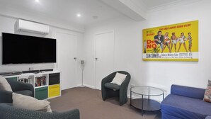 Una sala de estar moderna con un televisor de pantalla plana, una estantería, un sillón gris, una mesa de centro redonda de vidrio y un sofá azul.