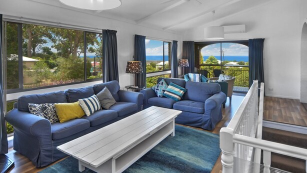 Una sala de estar moderna con un sofá azul, una mesa de centro blanca y vistas al mar a través de amplios ventanales.