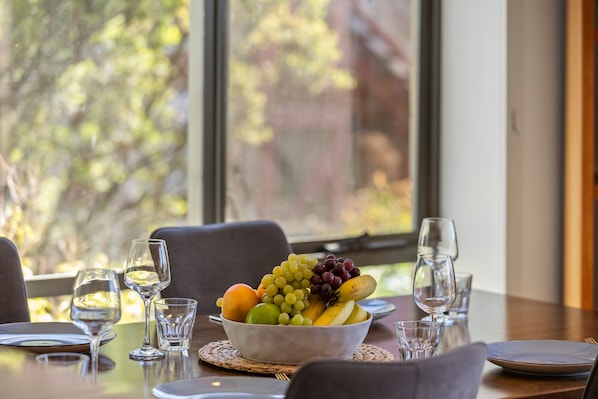 Una mesa de comedor con un bol de fruta, copas de vino y platos.