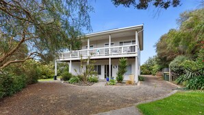 A two-story building with a balcony, surrounded by greenery and a gravel driveway.