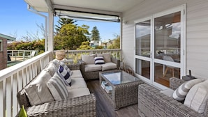 A covered outdoor seating area with wicker furniture and a glass table, overlooking a residential neighborhood.