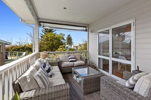 A covered outdoor seating area with wicker furniture and a glass table, overlooking a residential neighborhood.