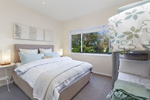 A bedroom with a bed, bedside lamps, a window with a view of trees, and a bunk bed.