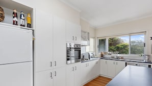 A modern kitchen with white cabinets, stainless steel appliances, and a view of the outdoors through a window.