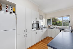 A modern kitchen with white cabinets, stainless steel appliances, and a view of the outdoors through a window.