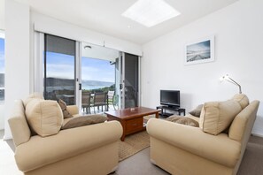 Ein modernes Wohnzimmer mit einer Sofagarnitur, einem Couchtisch, einem Fernseher und Blick ins Freie.
