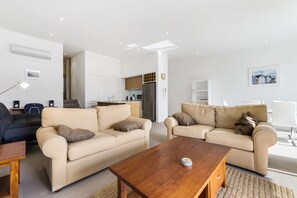 A modern living room with two beige sofas, a wooden coffee table, and a kitchen in the background. - Apollo Blue 11 (Apollo Bay)