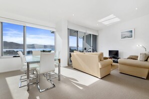 A modern living room with a sofa, a TV, and a dining area with chairs and a glass table. - Apollo Blue 11 (Apollo Bay)