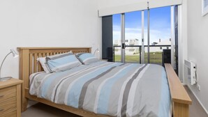 Ein Schlafzimmer mit einem hölzernen Bett, einem Nachttisch, einem Schreibtisch und einem großen Fenster mit Blick auf Gebäude.