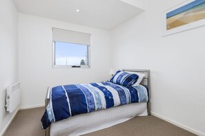 A bedroom with a bed, a window, a radiator, and a framed picture on the wall. - Apollo Blue 11 (Apollo Bay)