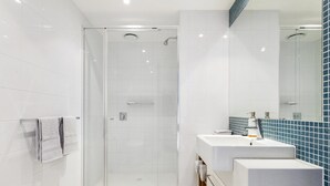 Ein modernes Badezimmer mit einer Duschkabine aus Glas, einem weißen Waschbecken inklusive Spiegel und einer blau gefliesten Rückwand.