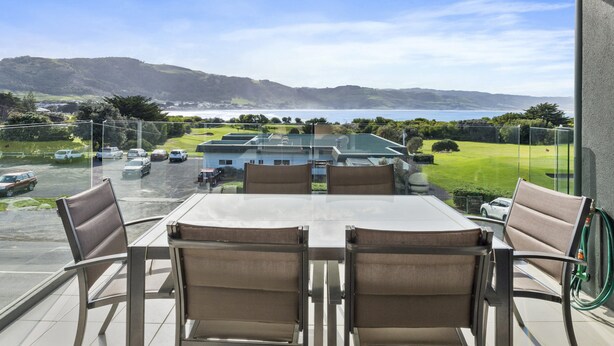 Ein Balkon mit Tisch und Stühlen mit Blick auf einen Golfplatz und ein Gewässer.