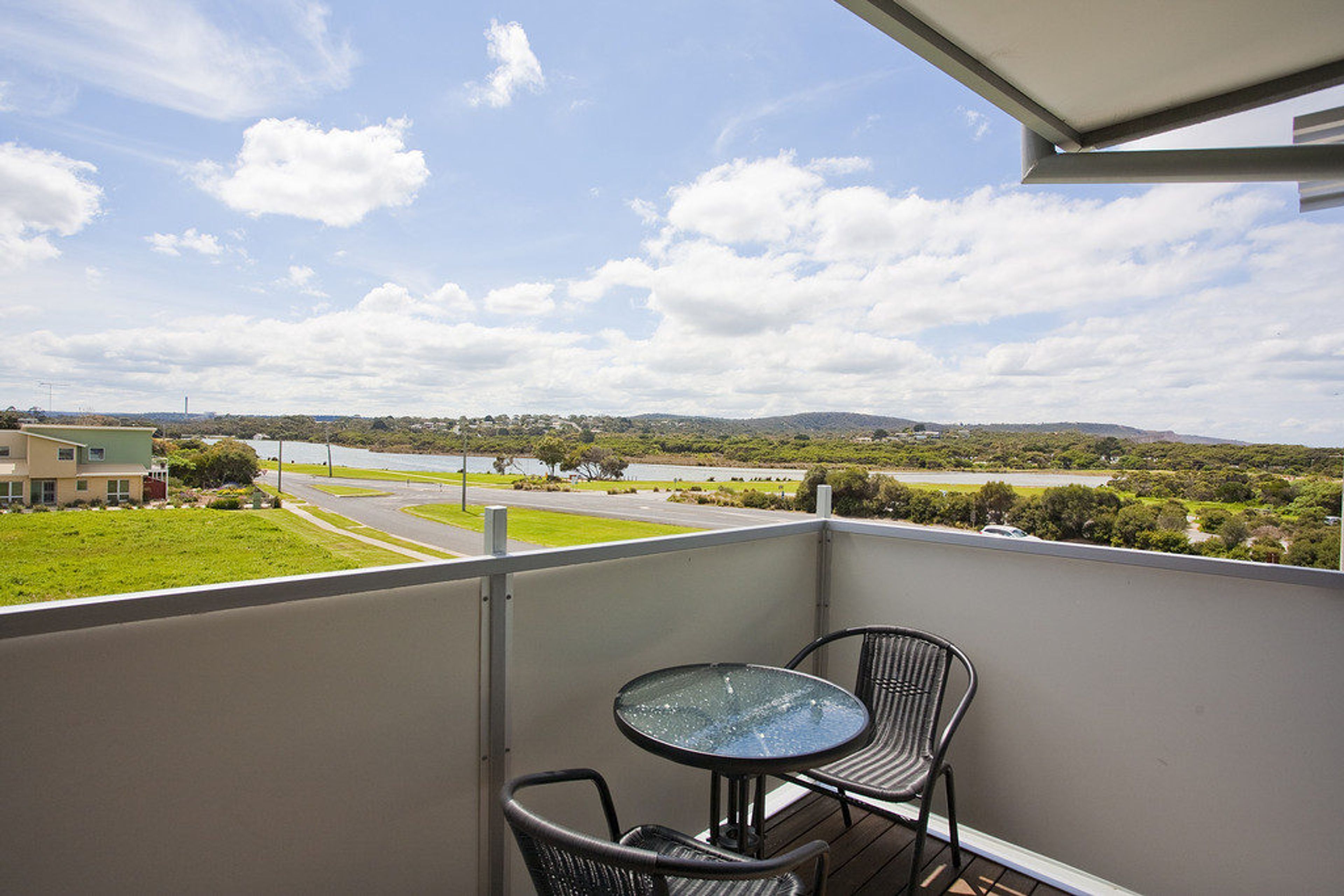 A balcony with a table and chairs, overlooking a road and greenery.