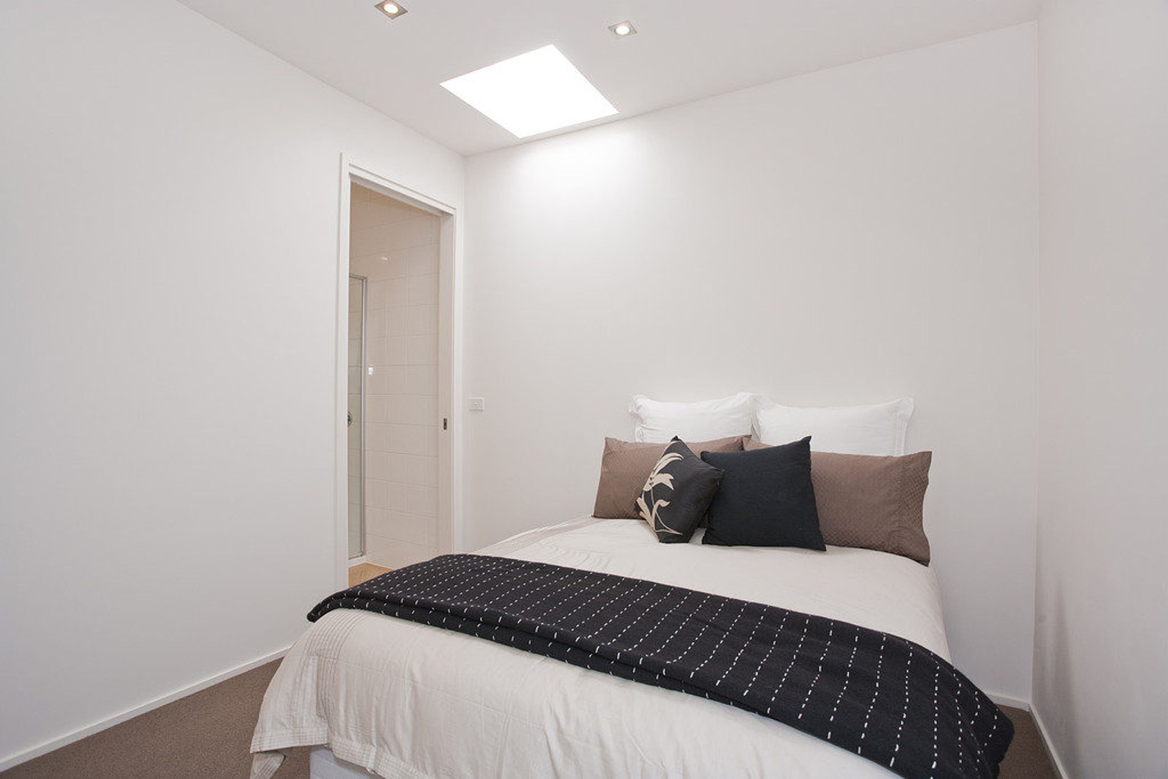 Quarto com cama, almofadas, mesa de cabeceira e porta que dá para um banheiro.