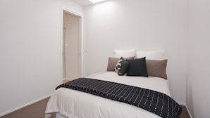 A bedroom with a bed, pillows, a bedside table, and a door leading to a bathroom. - Four Kings 3 (Anglesea)