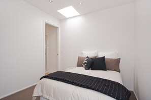 A bedroom with a bed, pillows, a bedside table, and a door leading to a bathroom. - Four Kings 3 (Anglesea)
