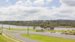 A road curving around a body of water with a residential area in the background. - Four Kings 3 (Anglesea)