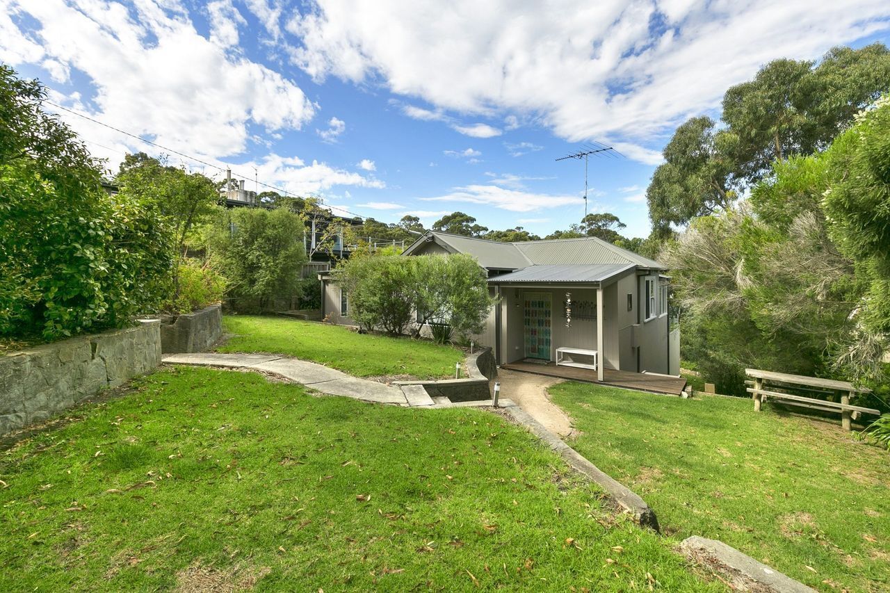 A residential property with a paved driveway, a front yard with a bench, and a house with a dark roof.