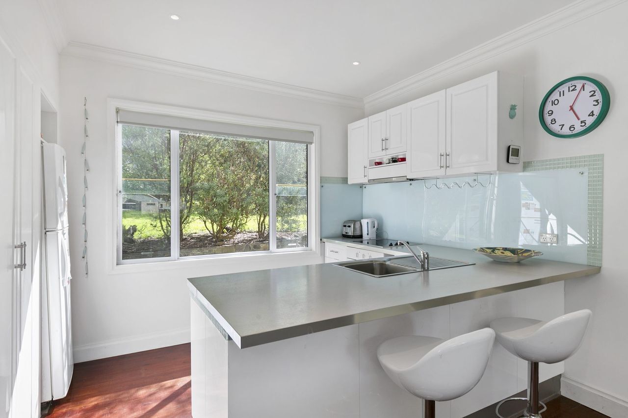 A modern kitchen with a large window, white cabinets, a stainless steel island, and two bar stools.