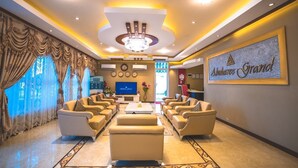 A spacious lobby with a chandelier, comfortable seating, a television, and a wall-mounted sign reading "Abuharee Grand". - Abuharee Grand (Hithadhoo)