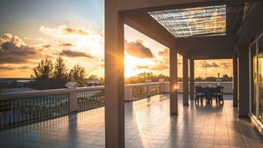 A covered outdoor area with a view of the sunset, a table with chairs, and a railing. - Abuharee Grand (Hithadhoo)