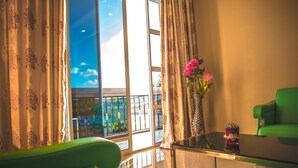 A room with a balcony, green chairs, a glass table, and a vase with flowers. - Abuharee Grand (Hithadhoo)