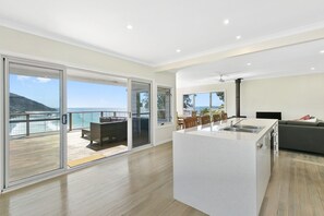 A modern interior with a kitchen island, dining area, and a balcony with a view of the sea.