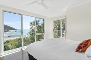 Ein Schlafzimmer mit einem großen Fenster, das Meer und Hügel zeigt.