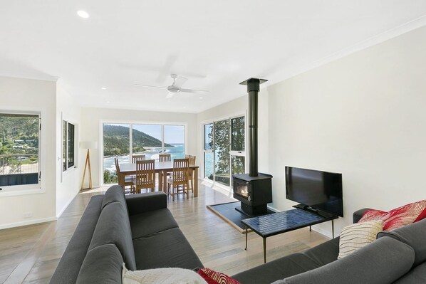 A modern living room with a sofa, a TV, a fireplace, and a dining area with a table and chairs.