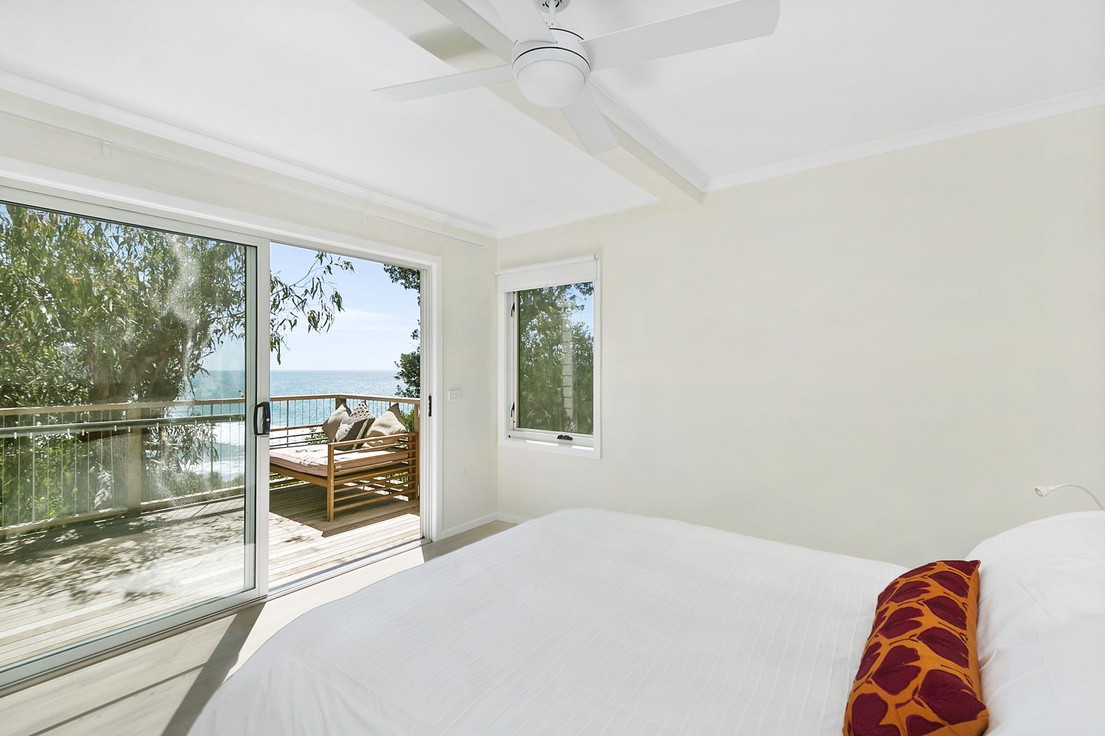 A bedroom with a large bed, a ceiling fan, and a view of a balcony with outdoor furniture.