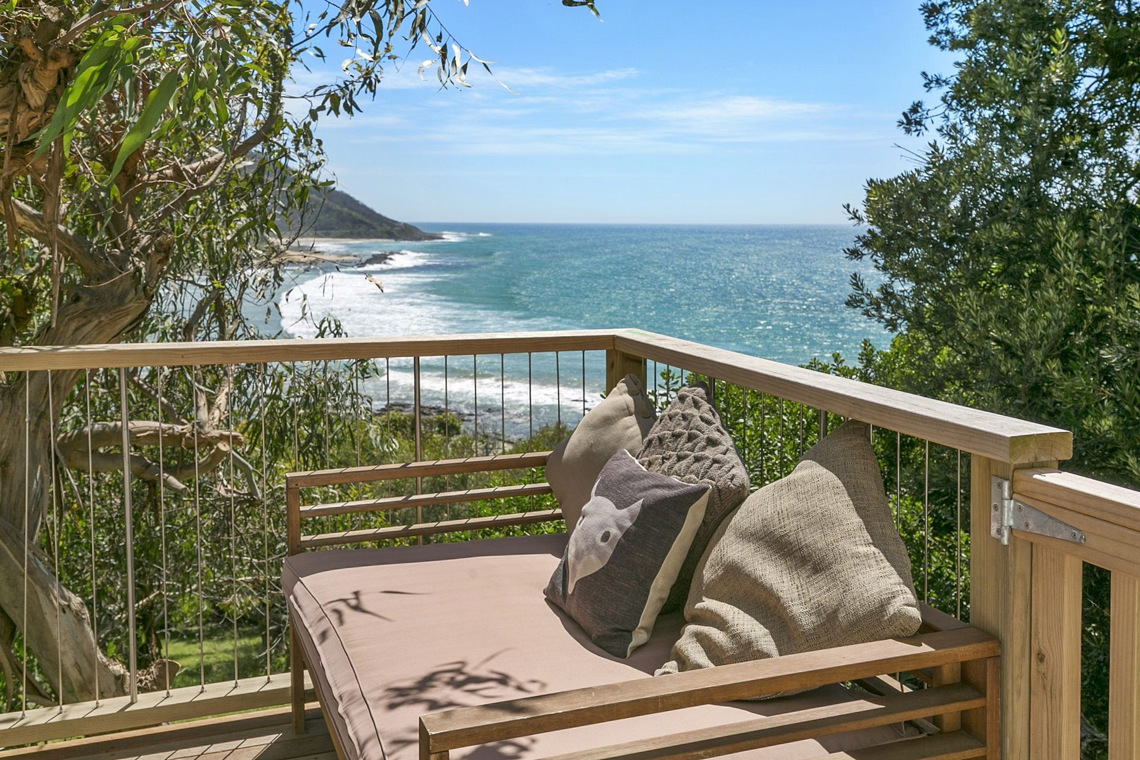 Eine Holzterrasse mit einer gepolsterten Sitzgruppe mit Blick auf einen Strand und den Ozean.