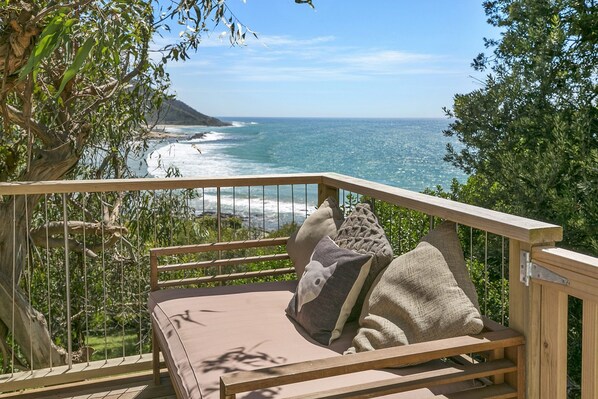 A wooden deck with a cushioned seating area overlooking a beach and ocean.