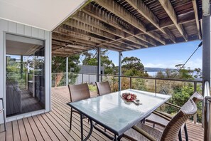 A covered outdoor area with a table and chairs, a glass door leading inside, and a view of the outdoors. - Scelta (Lorne)