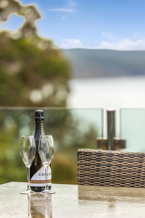 A bottle of Croser wine and two glasses on a table with a view of a lake and mountains in the background.