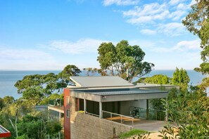 A modern house with a balcony overlooking a body of water, surrounded by greenery. - Scelta (Lorne)
