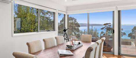 A spacious dining area with a large wooden table, six chairs, and a view of the sea through large windows.