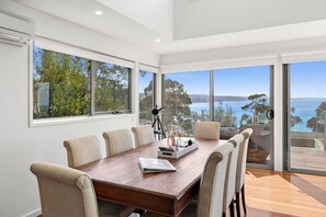 A spacious dining area with a large wooden table, six chairs, and a view of the sea through large windows. - Scelta (Lorne)