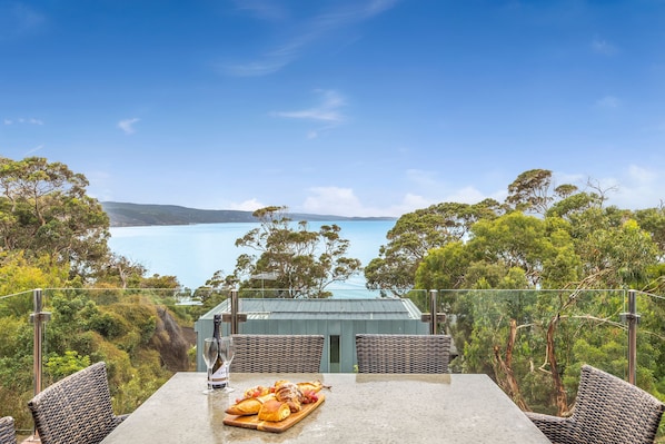 A dining table with a view of the sea, surrounded by greenery and overlooking a coastal landscape.