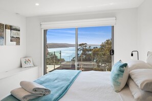 A bedroom with a large window, a bed with a blue blanket, and a view of the sea. - Scelta (Lorne)