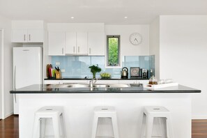 A modern kitchen with white cabinets, a black countertop, a sink, and three white stools. - Scelta Ask About Specials Wifi And Location (Lorne)