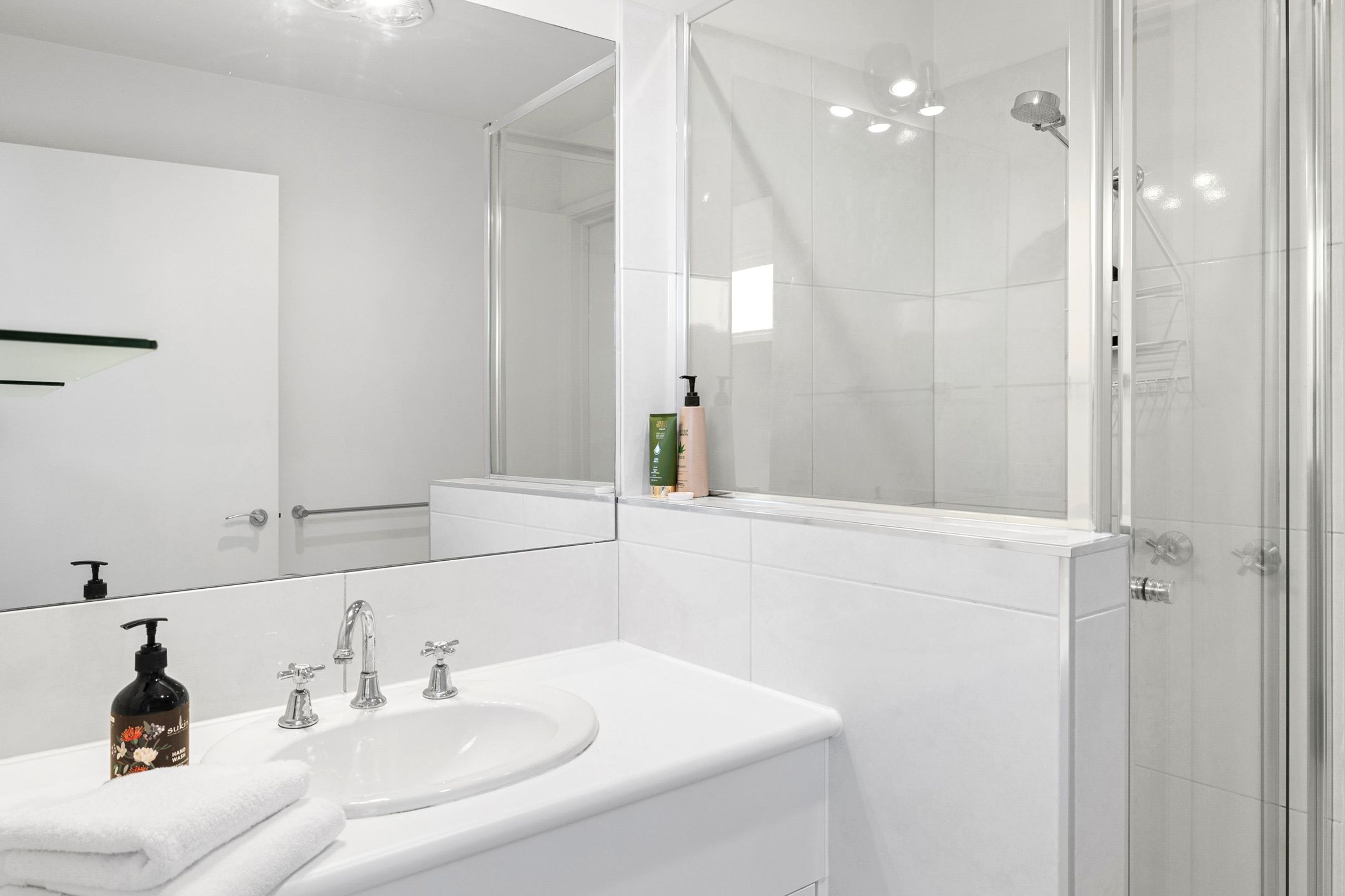 Een moderne badkamer met een wit wastafel, meerdere kraanwerk, een spiegel en een douchecabine van glas.