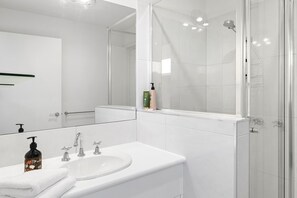 Un bany modern amb un rentapeus blanc, vària aixetes, un mirall i una cabina de dutxa de vidre.
