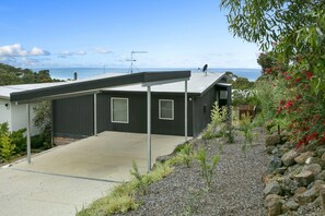 A modern house with a covered patio, a view of the sea, and a garden with rocks and plants.